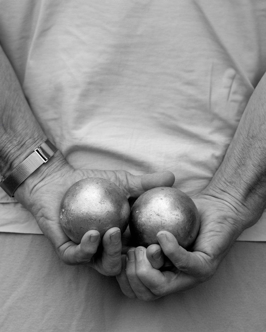 Man seen from behind holding two pétanque balls in his hands.
